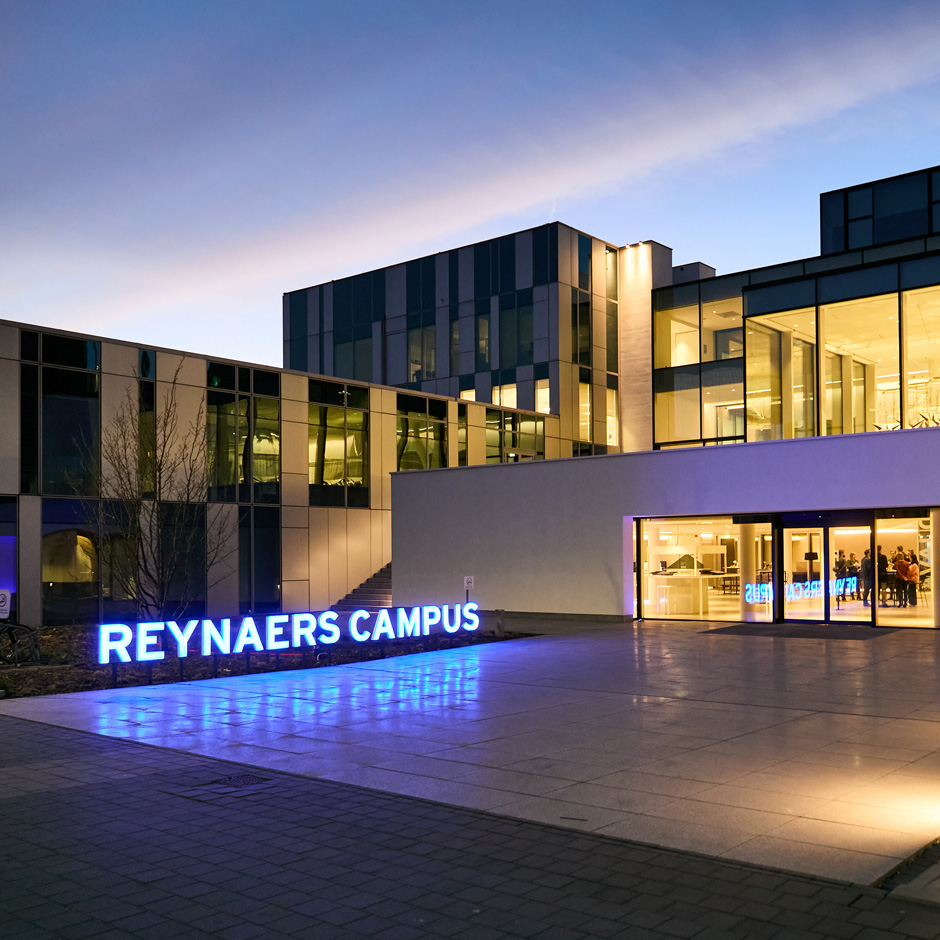 The Reynaers Campus at night, viewed from the back with lights shining bright within.