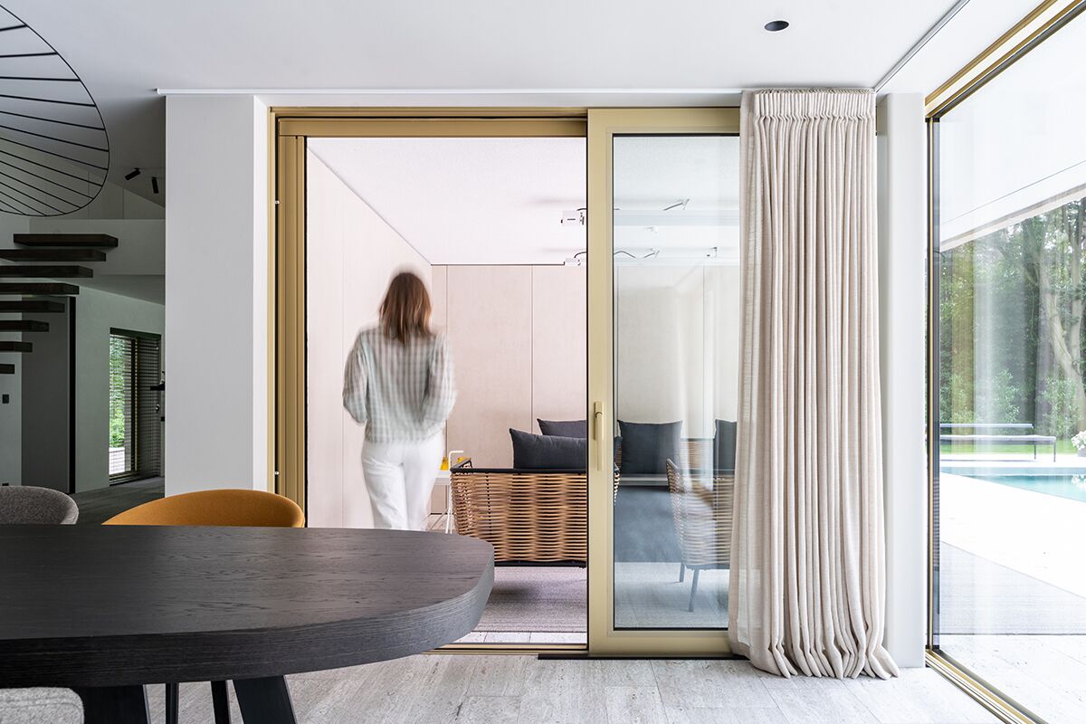 Frau, die moderne Villa durch goldene Schiebetüren betritt.