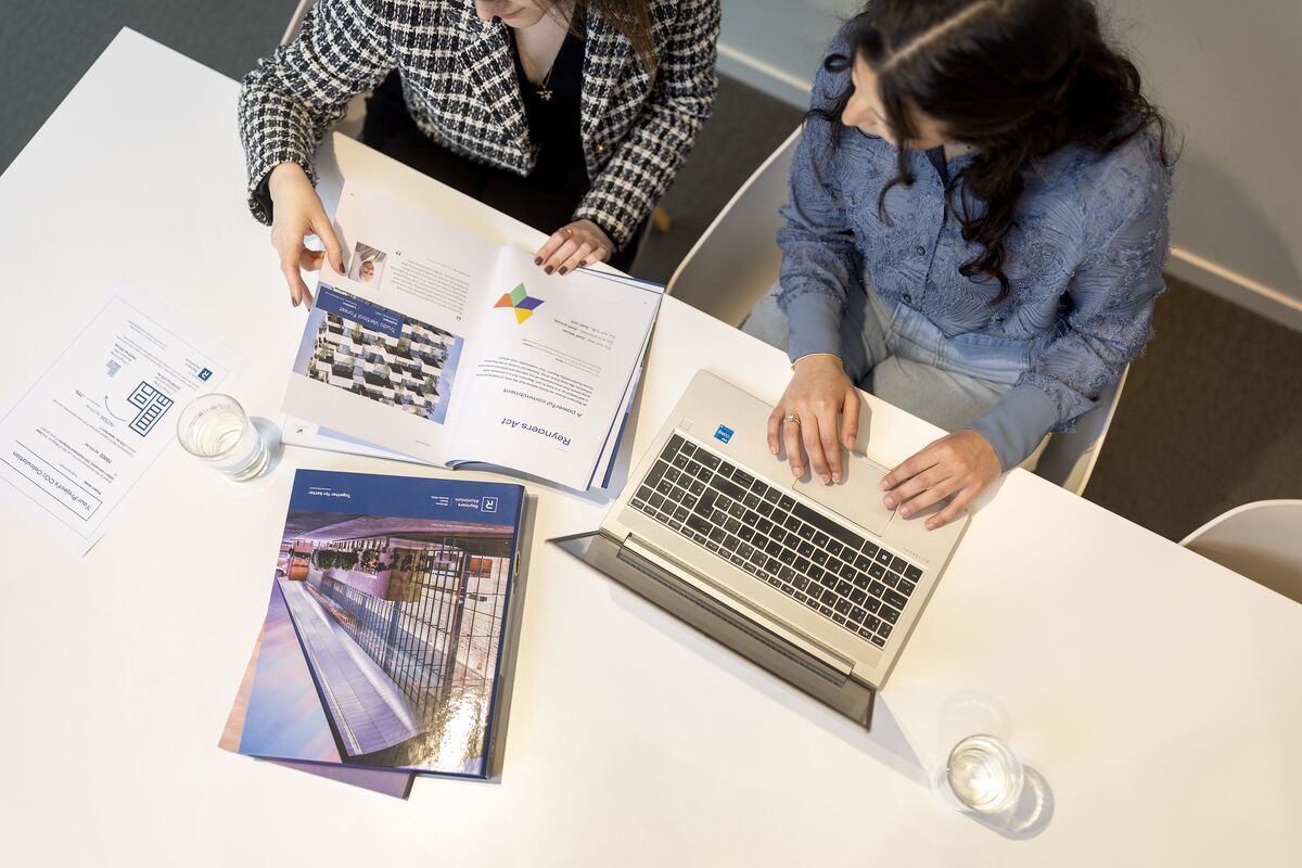 Draufsicht auf den Schreibtisch mit Papieren, Laptop und Ordnern.