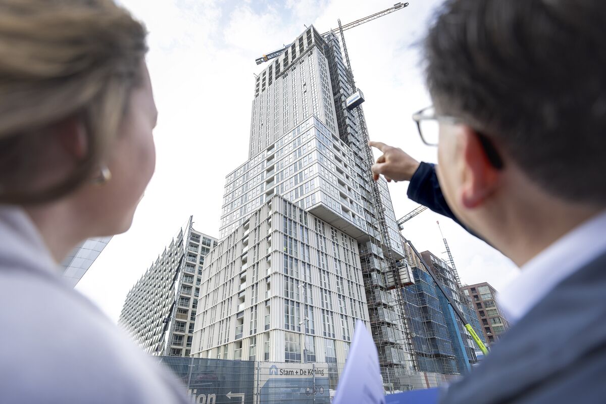 Mann und Frau schauen zu grauem Hochhaus im Bau auf.