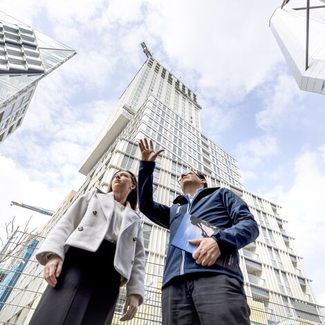 Mann und Frau zeigen auf Hochhäuser und reden über sie.