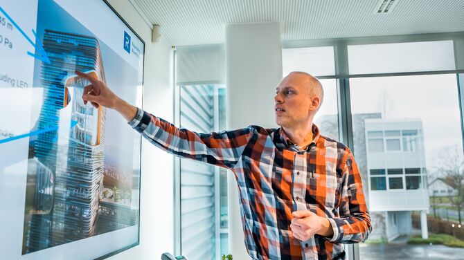 Weißer Mann im karierten Hemd zeigt auf den Präsentationsbildschirm.
