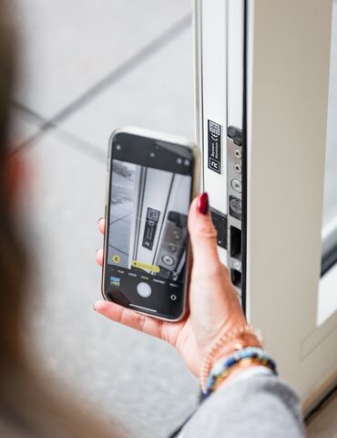 Hand hält Smartphone in der Nähe des QR-Codes auf weißem Fensterprofil.