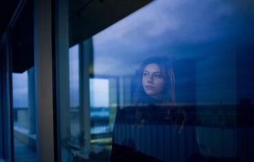 Frau, die bei Einbruch der Dunkelheit aus dem Fenster schaut.